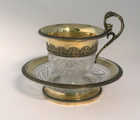 Französische Kristalltasse mit vergoldeter Silbermontierung. Tasse und 
Untertasse. Höhe 13 cm. Kleiner Stoss an der Tassenunterseite.